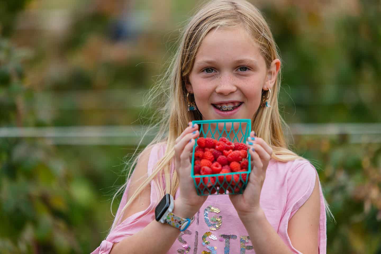 A young girl holding a basket of raspberries
