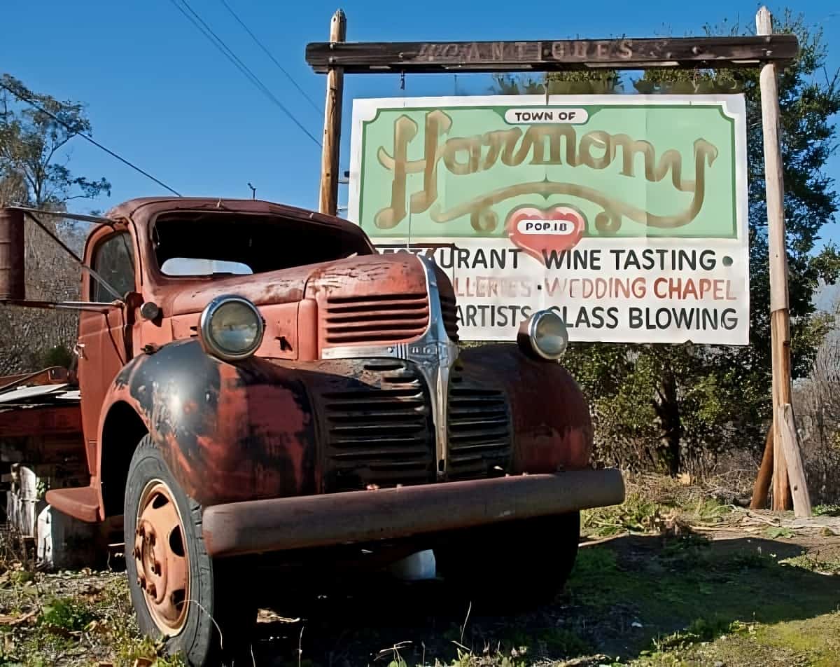Old truck in front of a sign for the town of Harmony, California