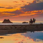 Horses and riders against a sunset on the beach in Cayucos